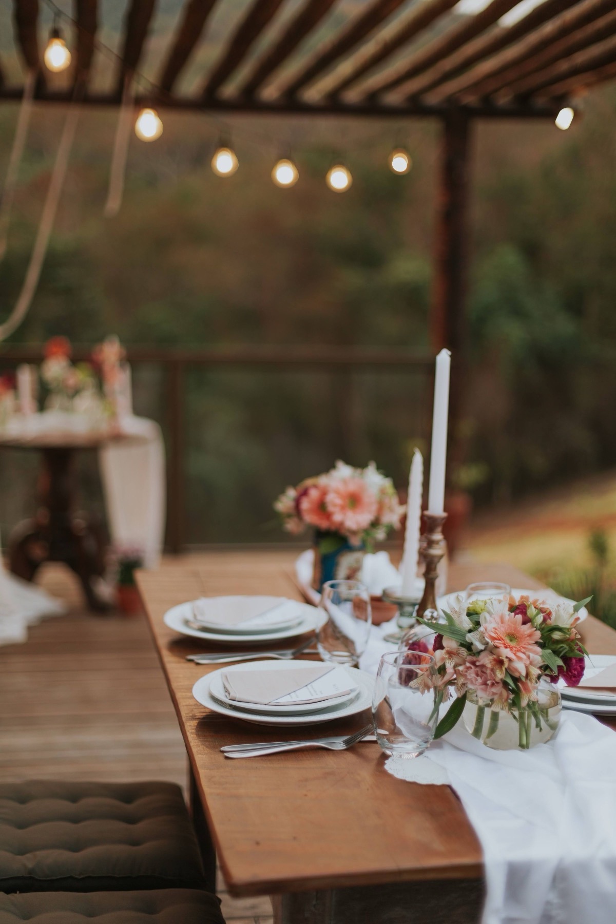 A long table laid for dinner under strings of warm lights at dusk.