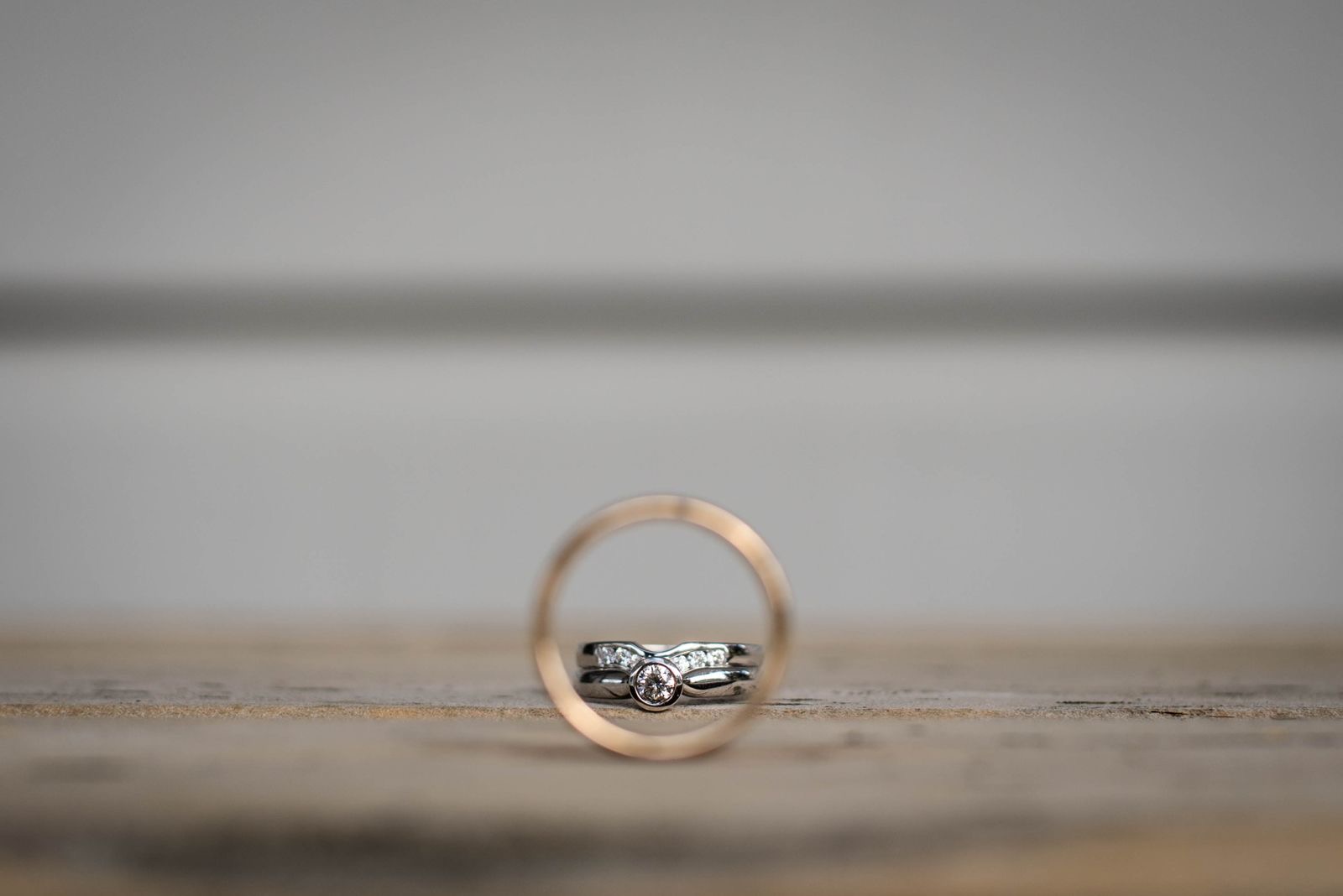 Two wedding rings resting on a pale table beside a folded ribbon.