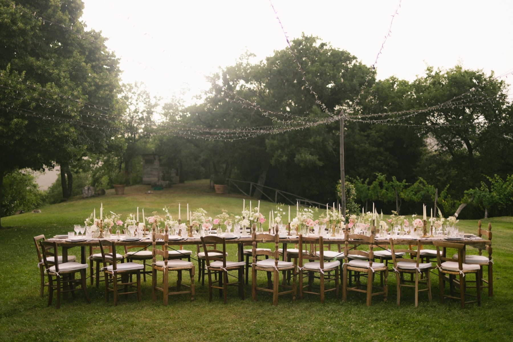 One long table set with candles and flowers in a field, every chair waiting.