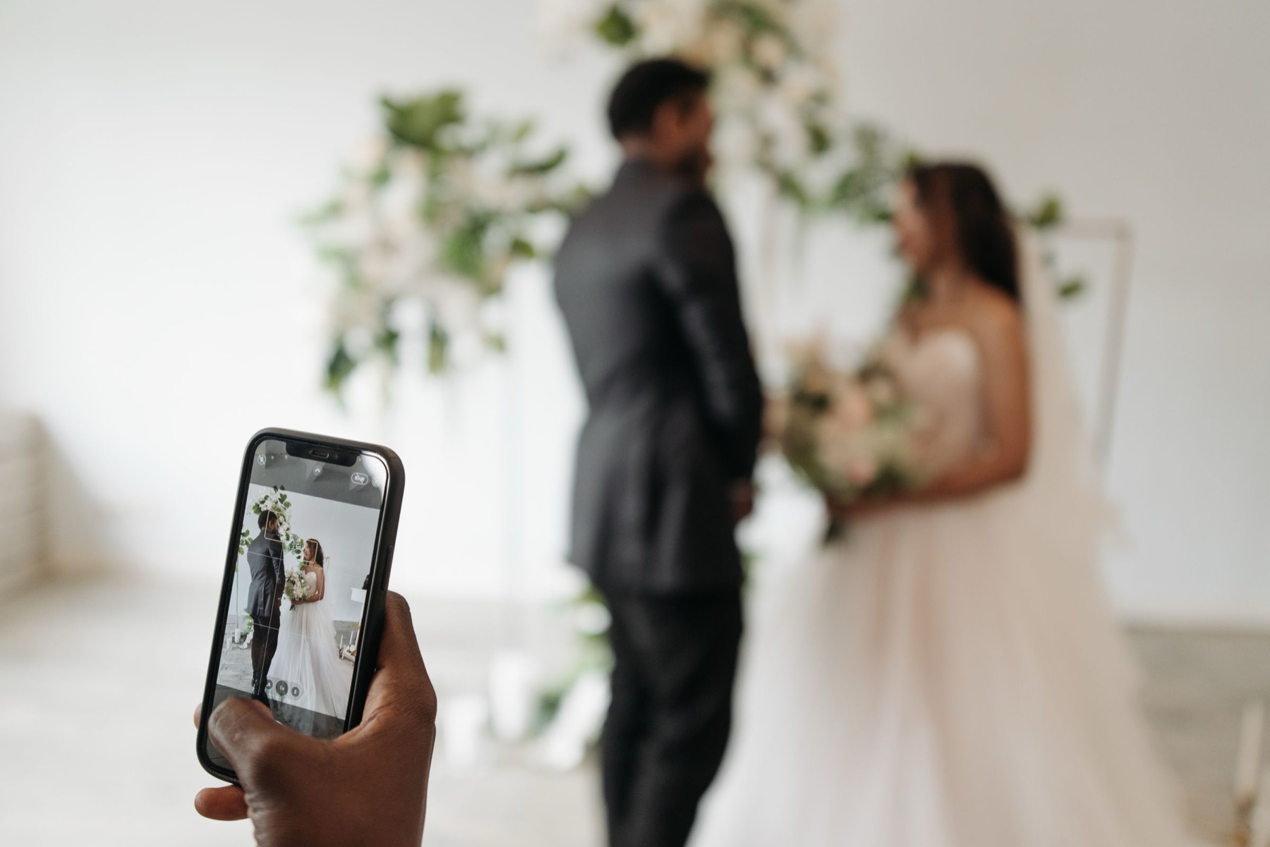 A guest holding up a phone to photograph a couple at their ceremony.